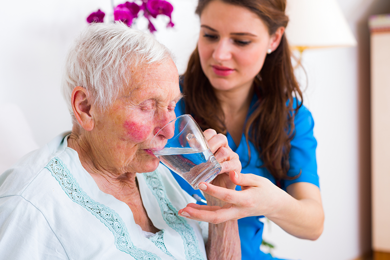 Nurse helping elderly patient drink water